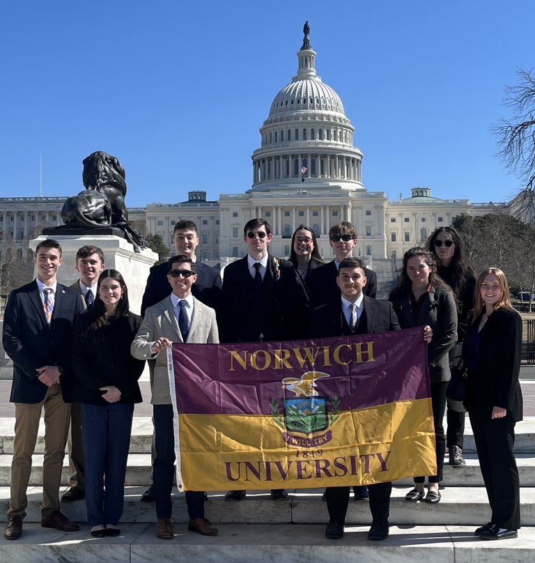 Eleven students hold a Norwich University flag in front of the U.S. Capitol.