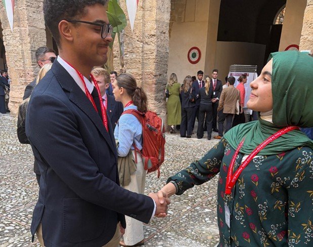 Two students wearing red lanyards shake hands in a stone courtyard.