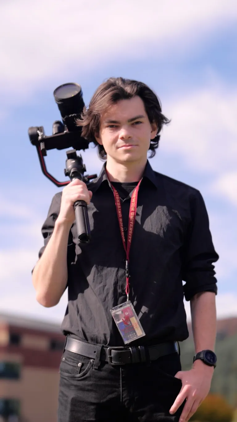 Student holds camera stabilizer outdoors while wearing a Norwich University lanyard.