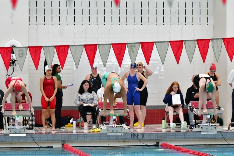 Swimmers prepare on starting blocks beside an indoor pool during a swim meet.