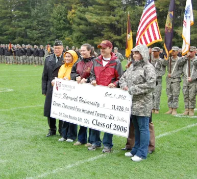 Five individuals stand on a football field holding a replica check.