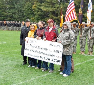 Five individuals stand on a football field holding a replica check.