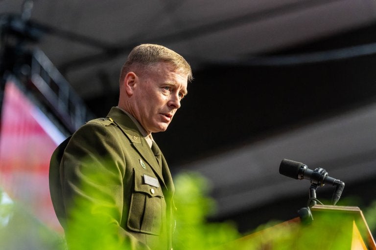 Military officer speaks at podium during indoor Norwich University ceremony.