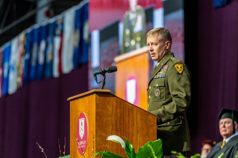 Military officer speaks at Norwich University podium during indoor ceremony.