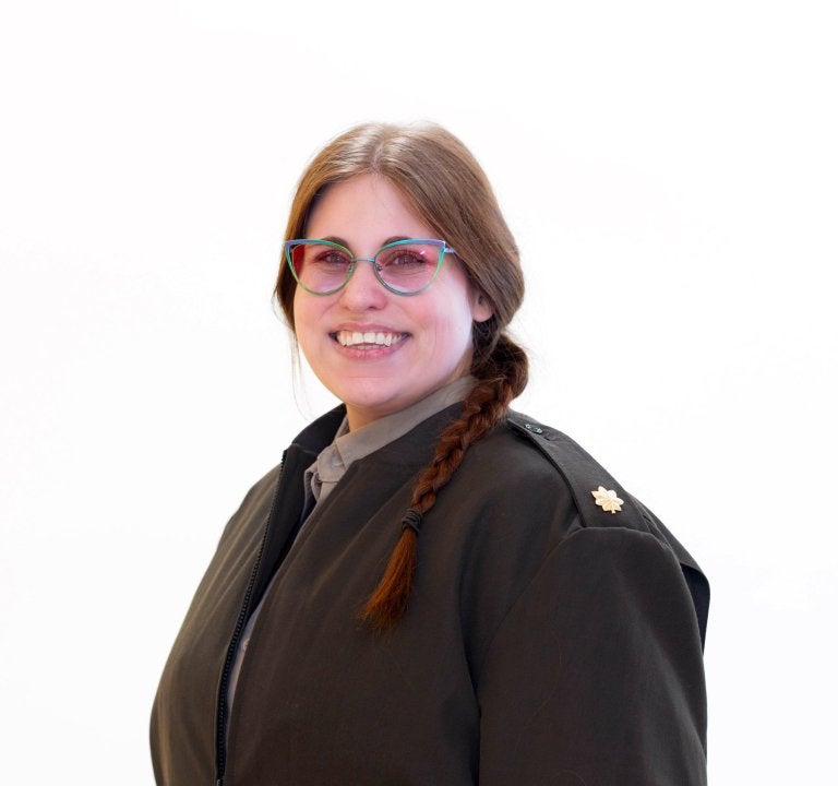 Person with glasses and a braid wears a dark coat and faces the camera.