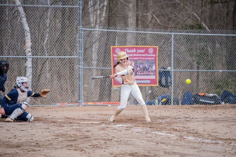 Softball player prepares to swing at a pitch while a catcher crouches behind home plate.