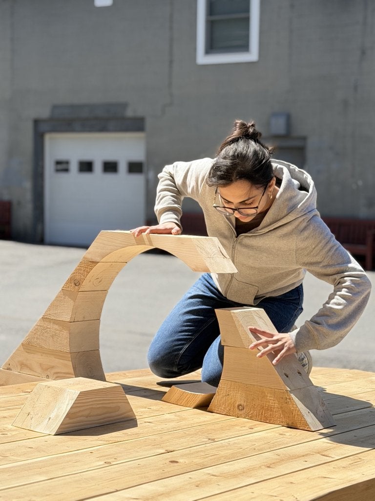 Person arranges curved wooden blocks on a wooden platform outdoors.