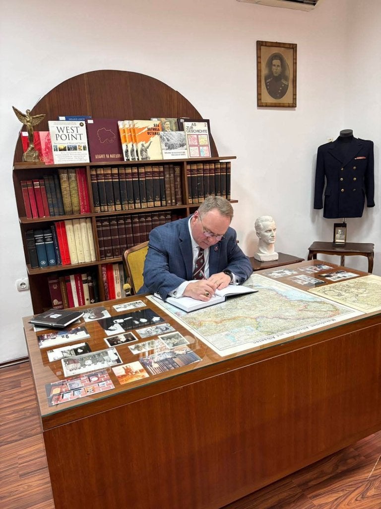 Person signs a guest book at a desk displaying maps, photographs, and historical items in a museum room.