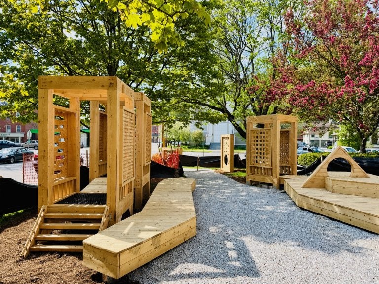 Wooden play structures and pathways stand among trees in a landscaped outdoor space.