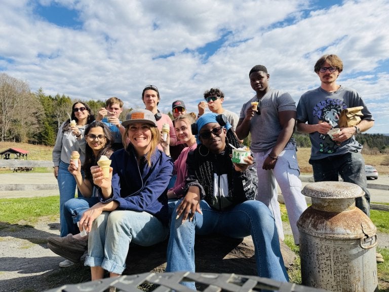 Students and an instructor hold ice cream cones while posing outdoors.