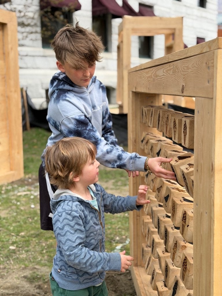 Two children turn wooden blocks on an interactive outdoor play wall.