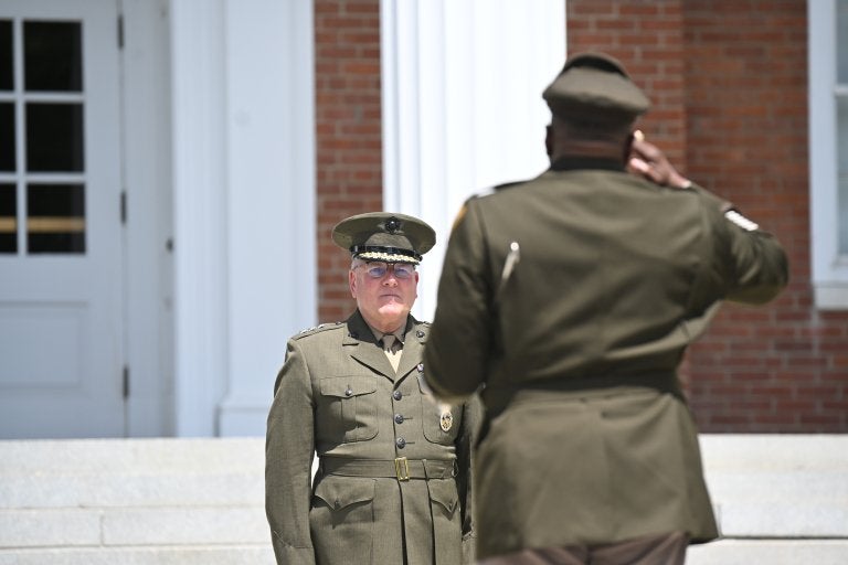 One uniformed officer salutes another during an outdoor military ceremony.