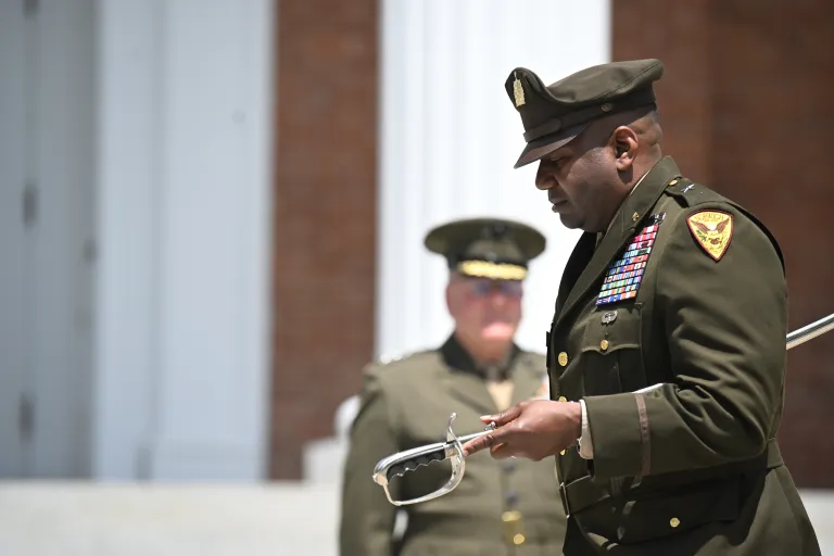 Uniformed officer holds a ceremonial sword during an outdoor military ceremony.
