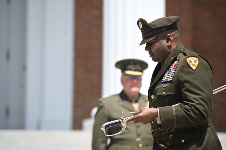 Uniformed officer holds a ceremonial sword during an outdoor military ceremony.