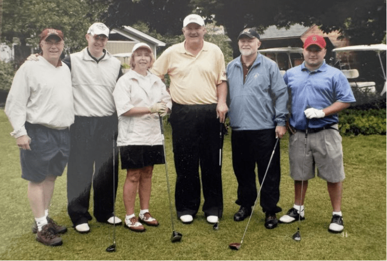 Six golfers pose with clubs on a grassy course near golf carts.