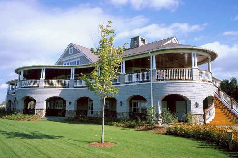 A large two-story building with arched openings to entrances lower level, and a wrap-around porch upper story. "National country Club, Shelburn, Vermont - Design development for Truex Cullins" by Michael McLean Architect is licensed under CC BY-SA 2.0.