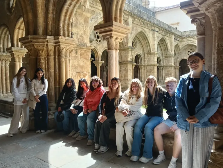 Group of students pose in a stone cloister with arched columns and vaulted walkways.