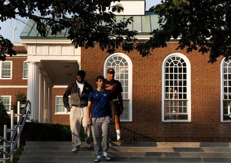 Three students walk down campus steps in front of a brick Chapel building with tall arched windows.