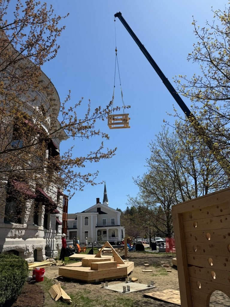 A crane lifts a wooden frame above a construction site with play structures below.
