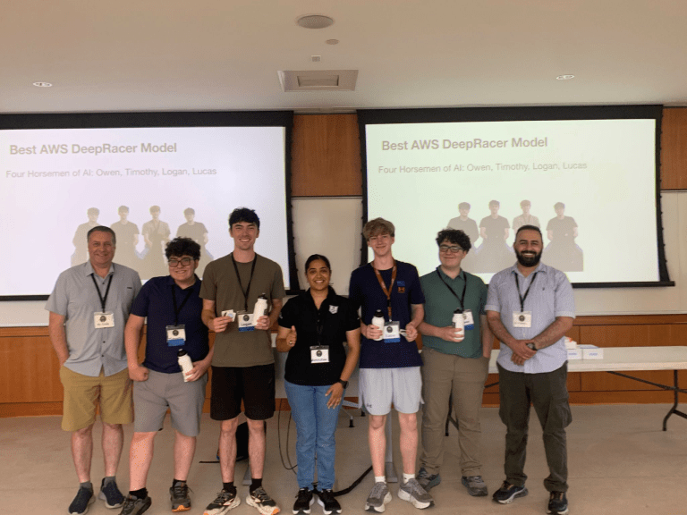 Group of students and instructors pose with water bottles in front of slides reading "Best AWS DeepRacer Model."