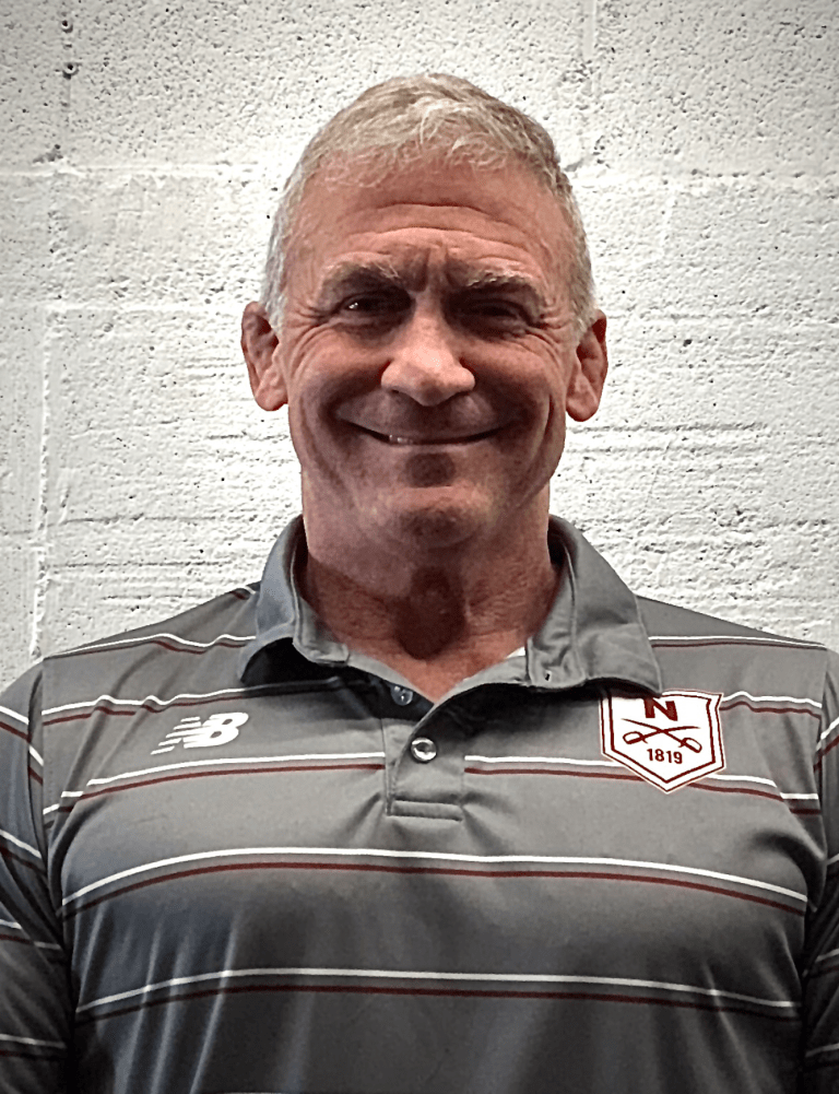Coach smiles in a striped Norwich polo shirt against a white brick wall.