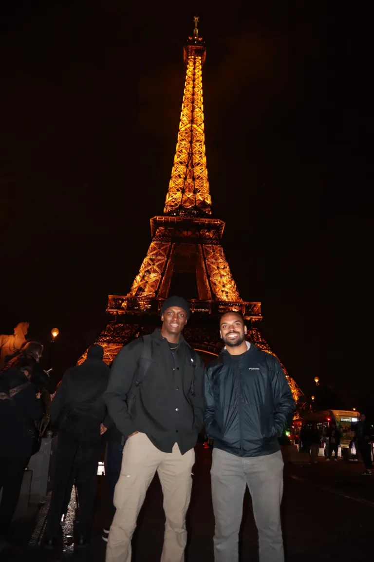 Two people stand in front of the illuminated Eiffel Tower at night.