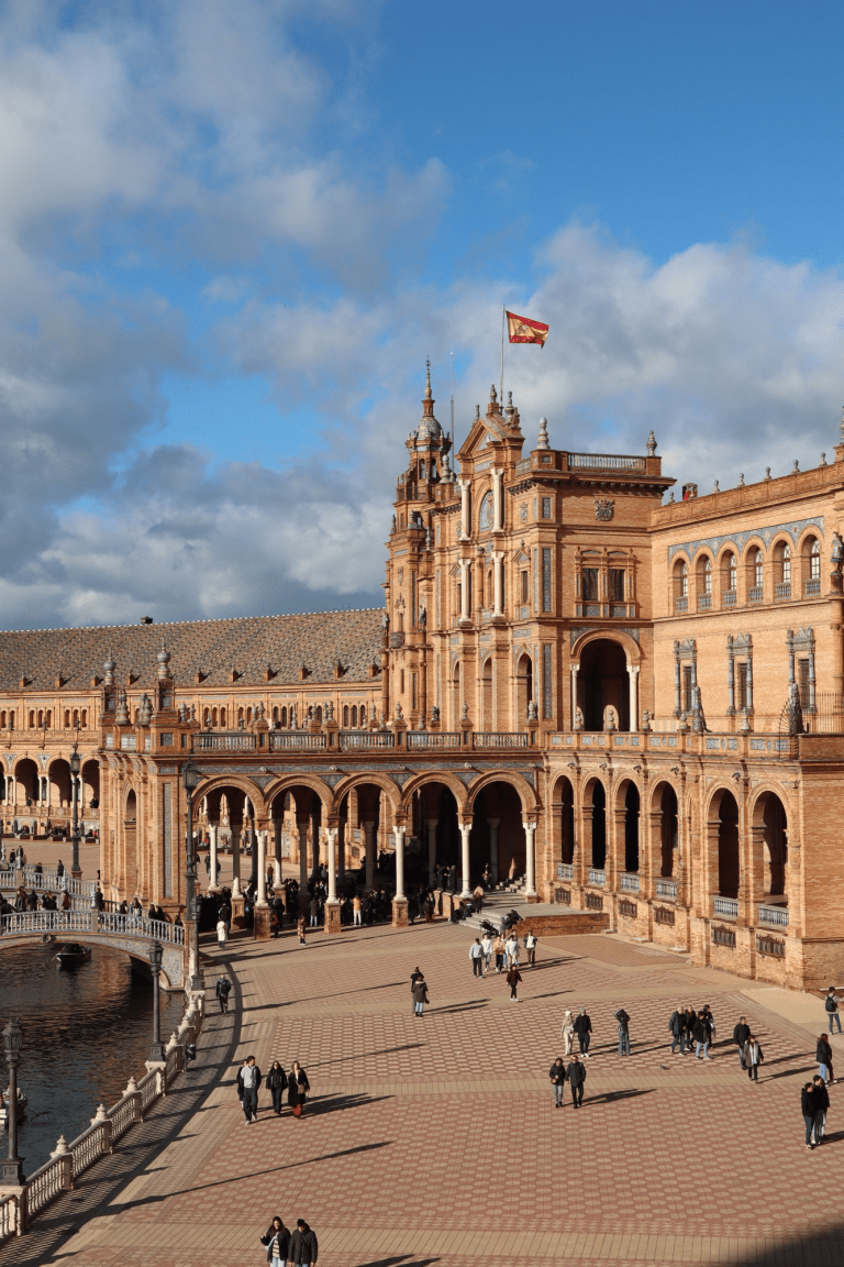 Plaza de España features arched walkways, a canal bridge, and a Spanish flag above the central building.