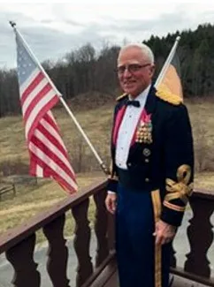 A man stands on a deck/porch with a US flag behind him.