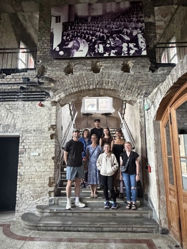 Eight people stand on stone steps beneath a brick archway inside a historic building.