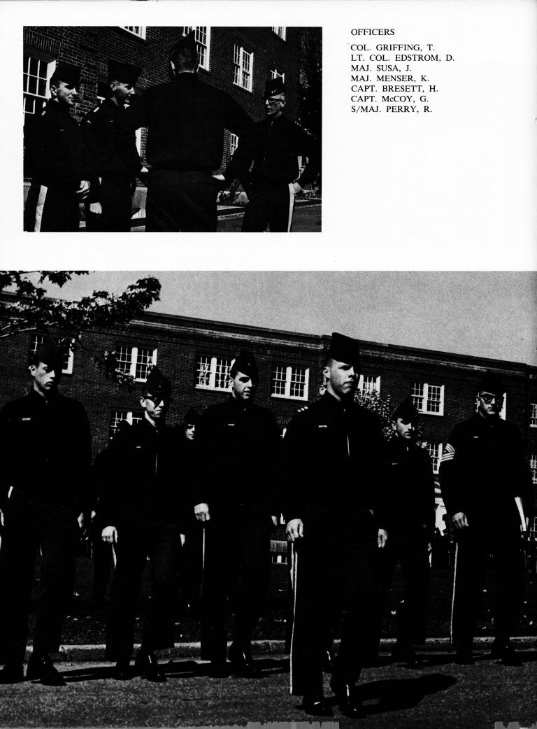 Cadets in uniform march in formation outside a brick building.