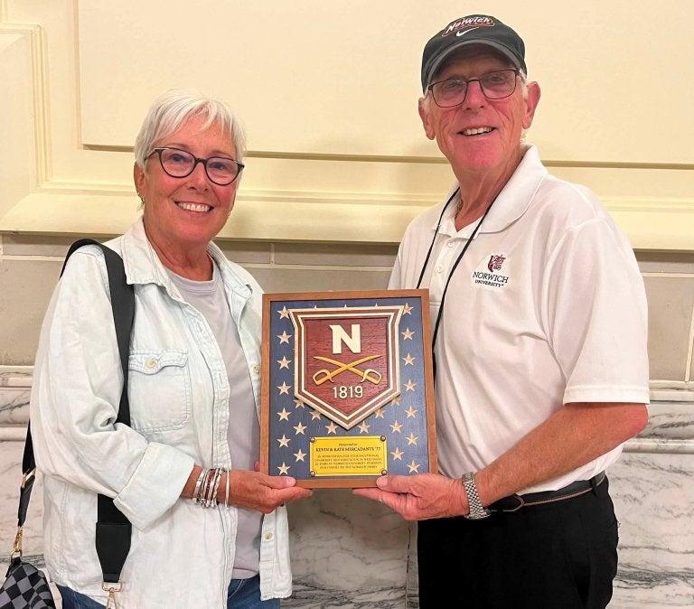 Two people hold a Norwich plaque with the University crest and 1819.