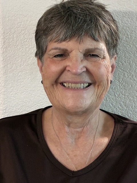 A person with short gray hair smiles at the camera against a light-colored wall.