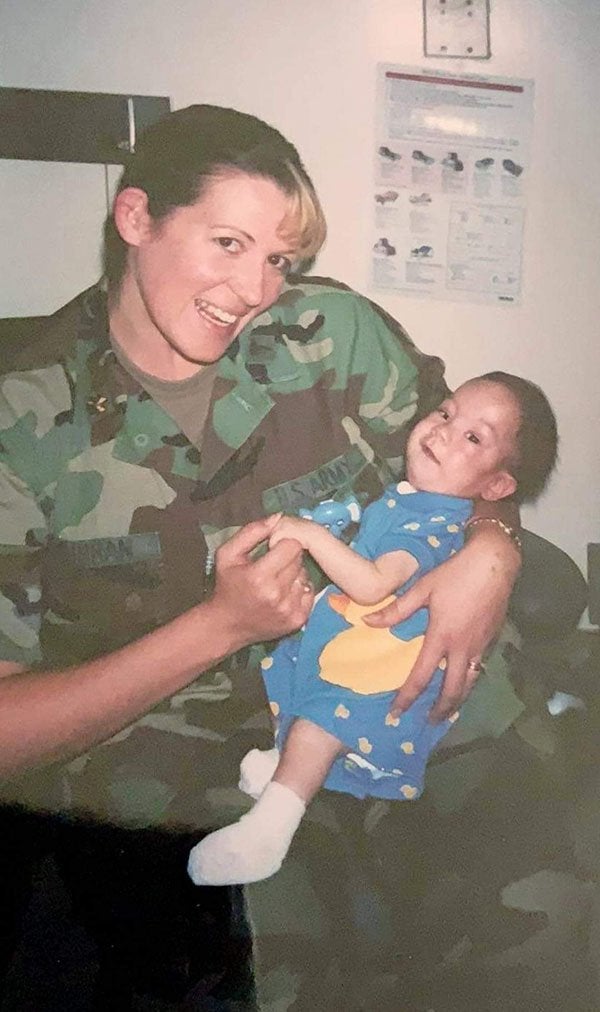 A service member in camouflage holds an infant indoors.