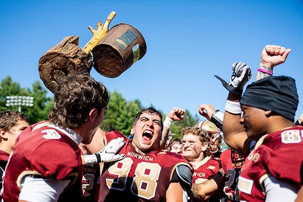 Norwich football players celebrate as one player holds a broken wooden trophy overhead.