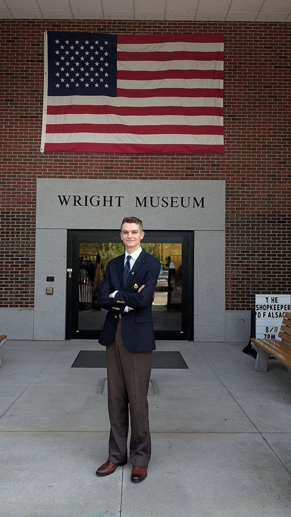 A person in a blazer stands beneath a large U.S. flag outside the Wright Museum.