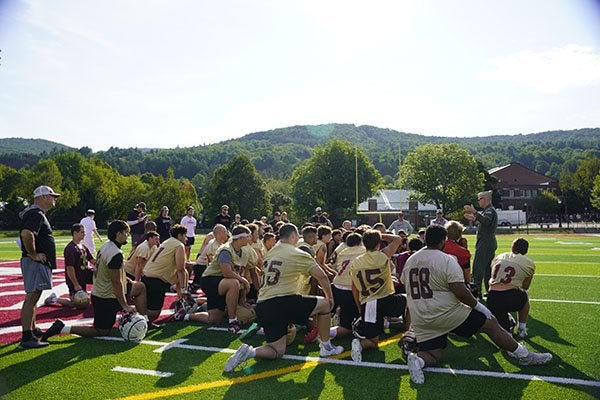 Football players kneel on the field around a coach speaking to the team.