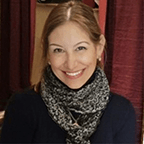 Person wearing a dark scarf and black top poses in front of red curtains.