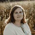 Person wearing a light cardigan stands outdoors in front of a field.