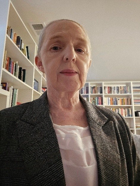 A person in a blazer poses indoors with bookshelves in the background.
