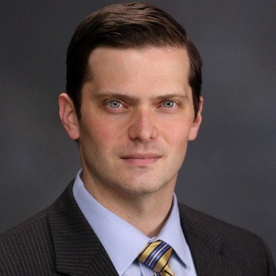 A person in a suit and striped tie poses against a dark gray background.