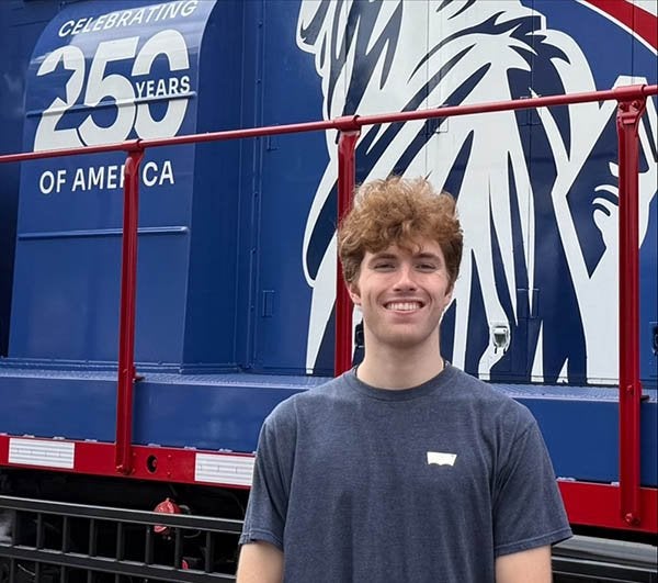 A person stands in front of a blue and red train marked "Celebrating 250 Years of America."