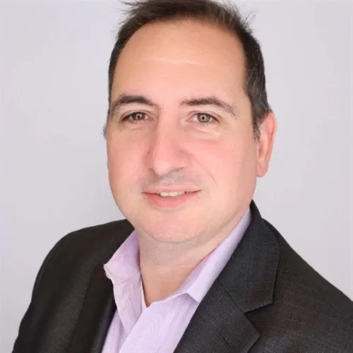A person in a dark blazer and light collared shirt poses against a light gray background.