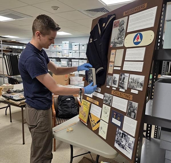 A person wearing gloves places an artifact on a museum exhibit about messengers and collecting.