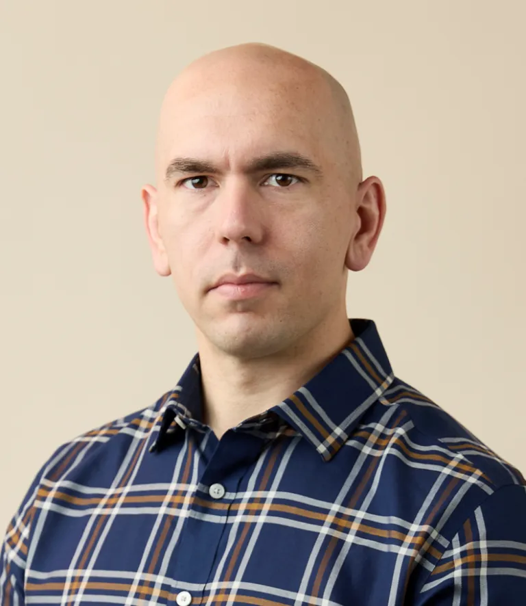 A person in a blue plaid collared shirt poses against a light beige background.