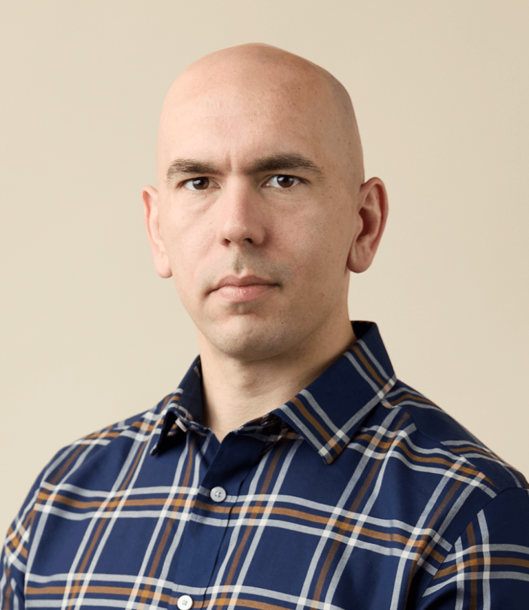 A person in a blue plaid collared shirt poses against a light beige background.