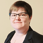 Person wearing glasses and a dark blazer poses against a light background.