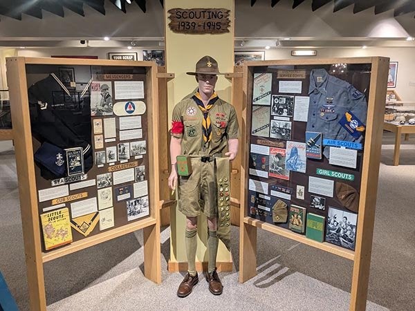 A museum exhibit displays a Scout uniform and artifacts beneath a sign reading "Scouting 1939-1945."