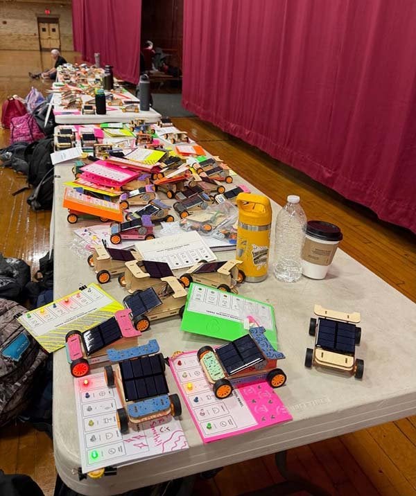 Tables display student-built solar-powered model cars, project materials, and worksheets.