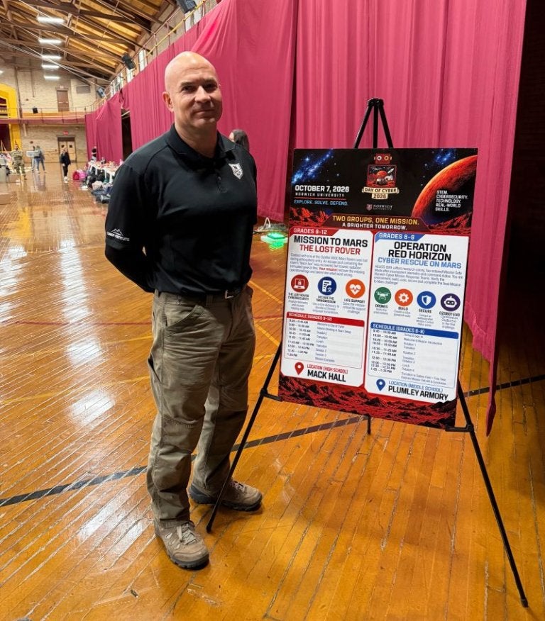 A person stands beside a Day of Cyber 2026 event sign featuring two Mars-themed cybersecurity challenges.