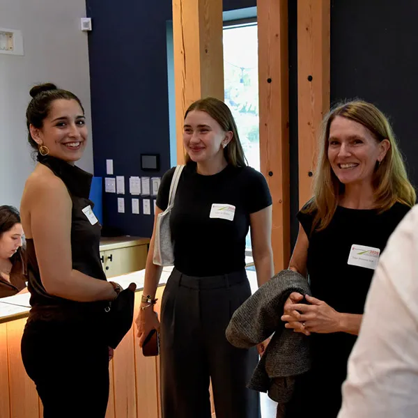 Three people wearing name tags stand together and smile during an indoor event.